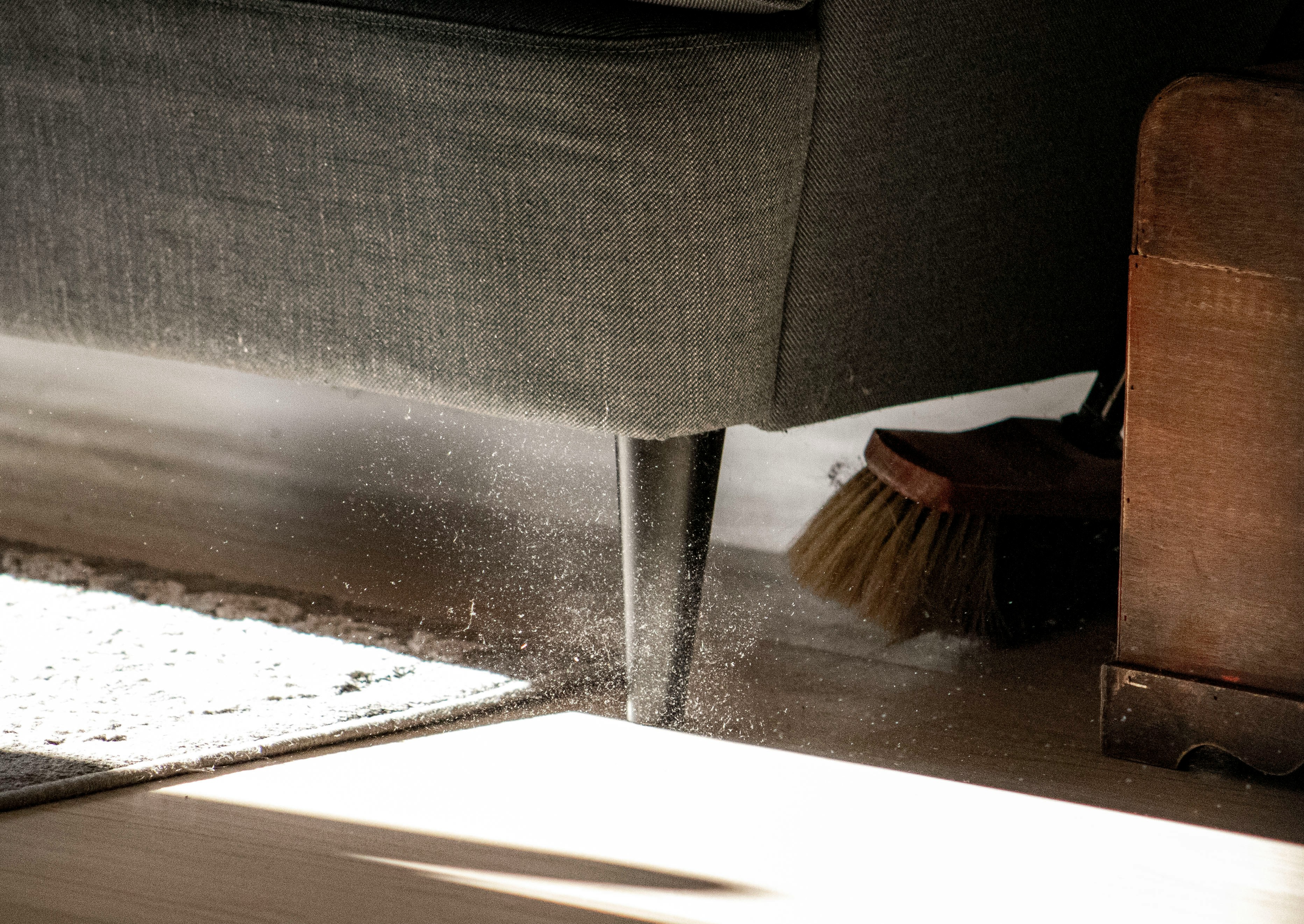 close up of a couch leg with a broom sweeping dust 